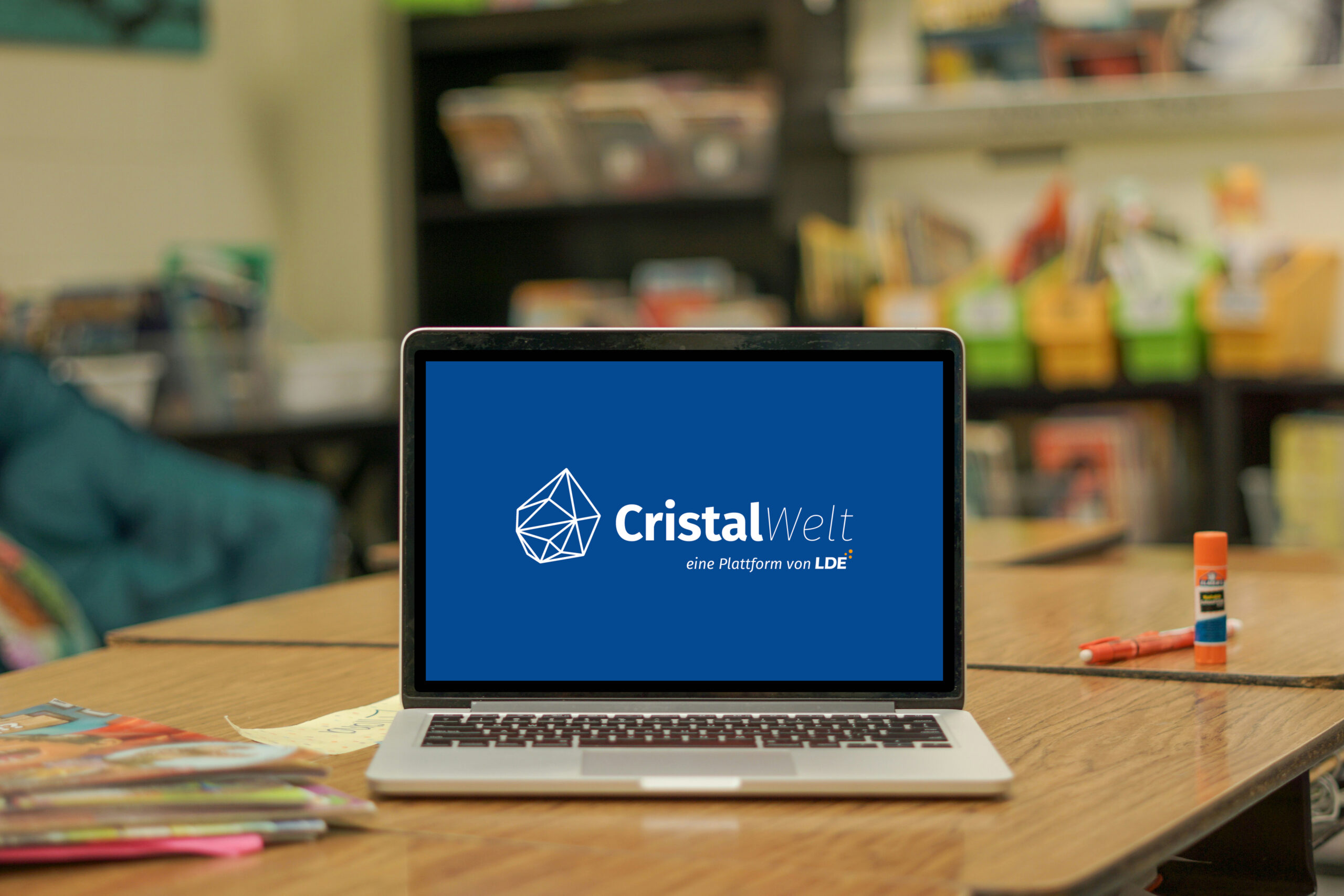Computer auf einem Tisch. Im Hintergrund das Logo unseres Kundenbereichs: die Cristal-Welt.
